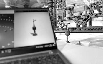 Schwarz-Weiß-Bild eines Laptops mit einem 3D-Modell auf dem Bildschirm, im Hintergrund ein kunstvoll gestaltetes Geländer.