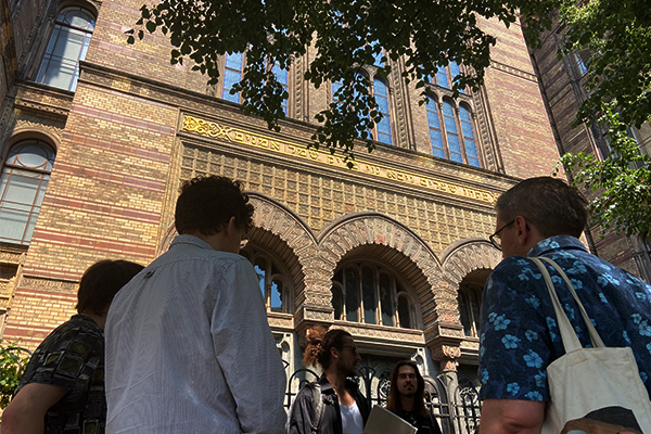 Gruppe von Personen steht vor der Synagoge, betrachtet die Architektur und hört einer Führung zu.